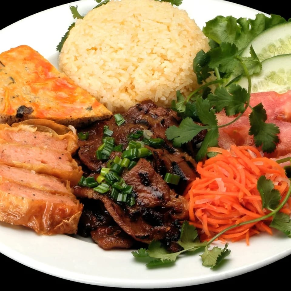 Vietnamese dish with grilled meat, rice, pickled carrots, egg cake, and fresh vegetables.