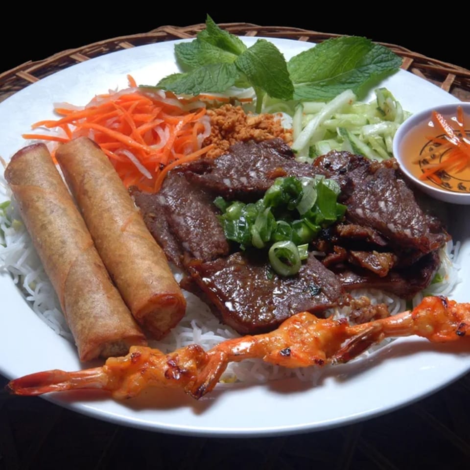 Vietnamese vermicelli bowl with grilled beef, shrimp, egg rolls, and fresh vegetables.