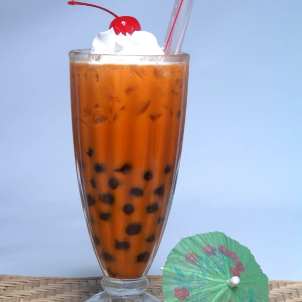 Vietnamese bubble tea with whipped cream, a cherry, and a green paper umbrella.