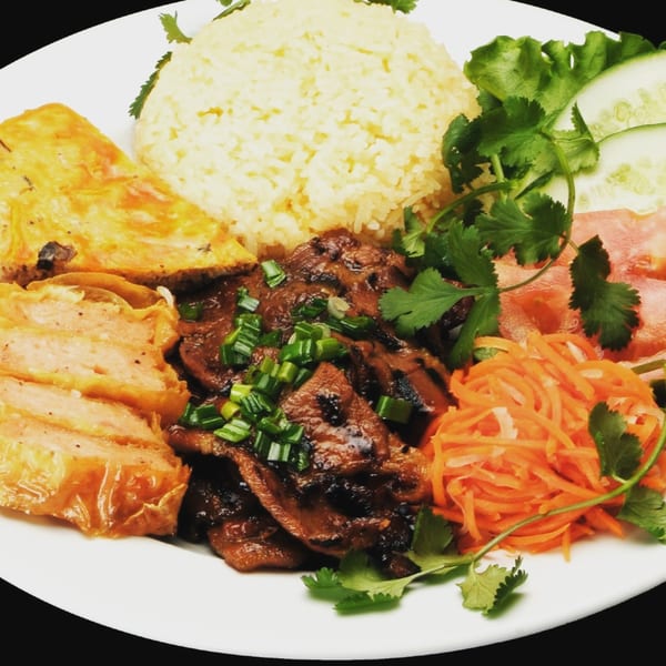 Vietnamese grilled pork, fried egg cake, rice, pickled carrots, and fresh vegetables on a white plate.