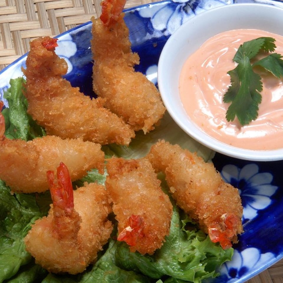 Crispy fried shrimp on lettuce with a side of pink dipping sauce garnished with cilantro.