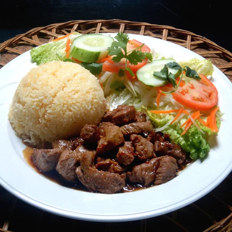 Vietnamese dish with rice, stir-fried beef, and a fresh salad with cucumbers and tomatoes.