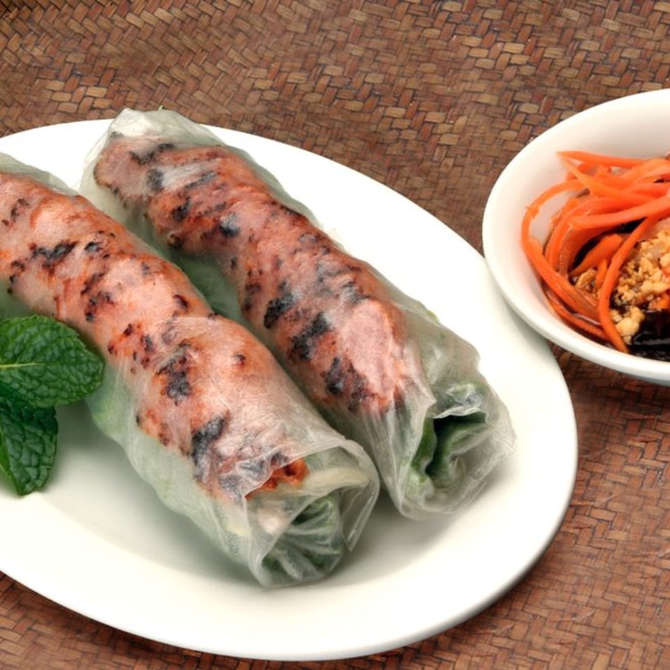 Two Vietnamese spring rolls with grilled pork and mint, served with a side of pickled carrots.