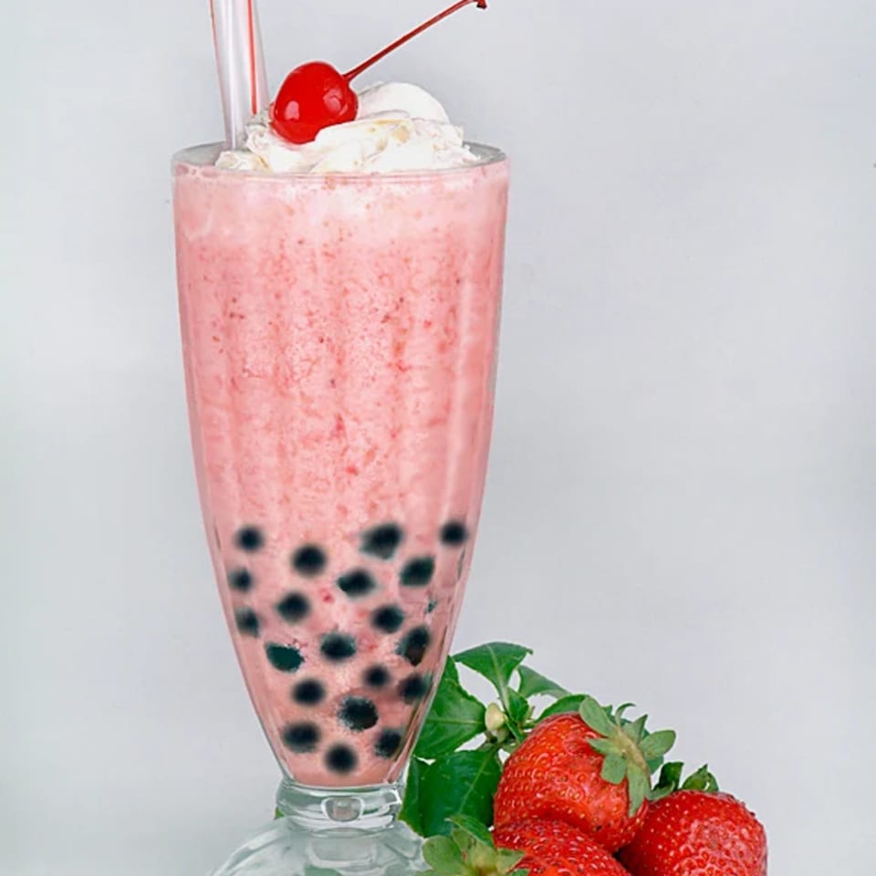 Strawberry boba smoothie with whipped cream, a cherry, and fresh strawberries on the side.